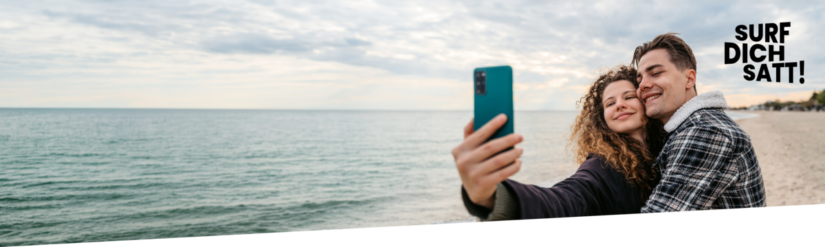 Junges Paar macht ein Selfie am Strand und nutzt einen Handytarif mit Handy
