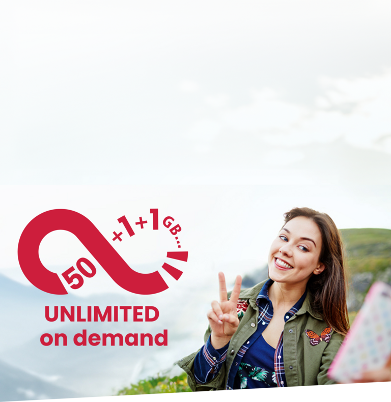 Eine junge Frau zeigt das Peace-Zeichen und macht mit ihrem Handy und unbegrenztem Datenvolumen ein Selfie an einer Klippe.