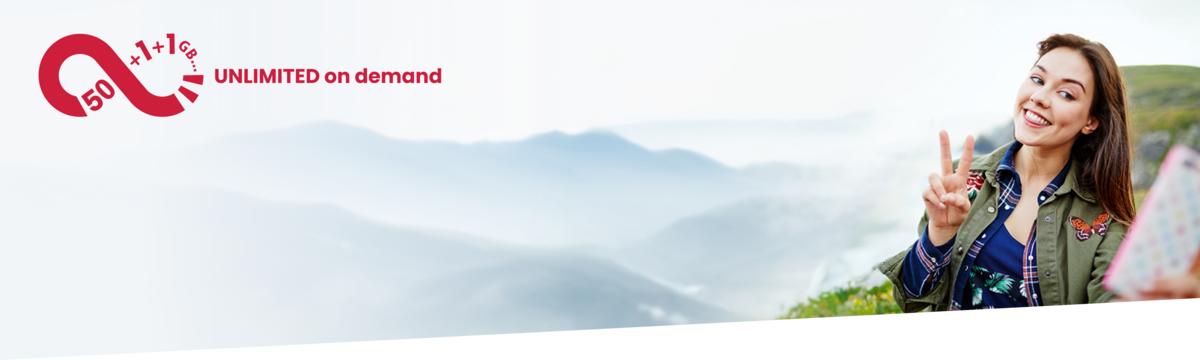 Eine junge Frau zeigt das Peace-Zeichen und macht mit ihrem Handy und unbegrenztem Datenvolumen ein Selfie an einer Klippe.